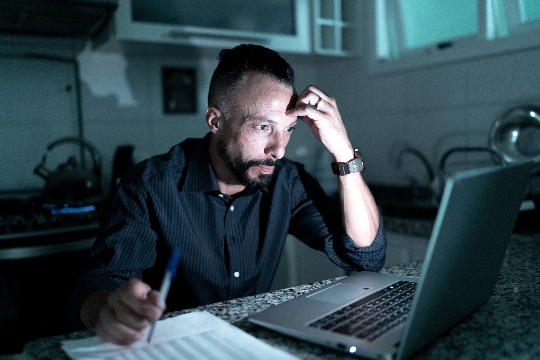 A stressed investor looks at his laptop while working at his desk late at night.