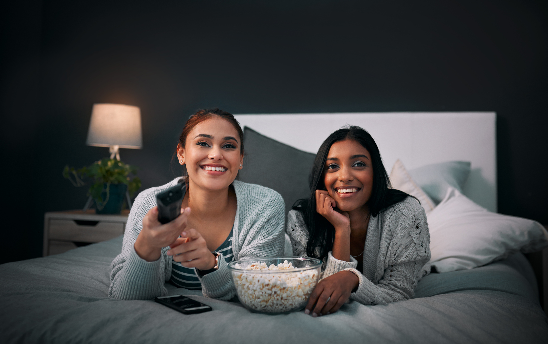 Two people sitting on a bed watching TV with a smile on their faces.