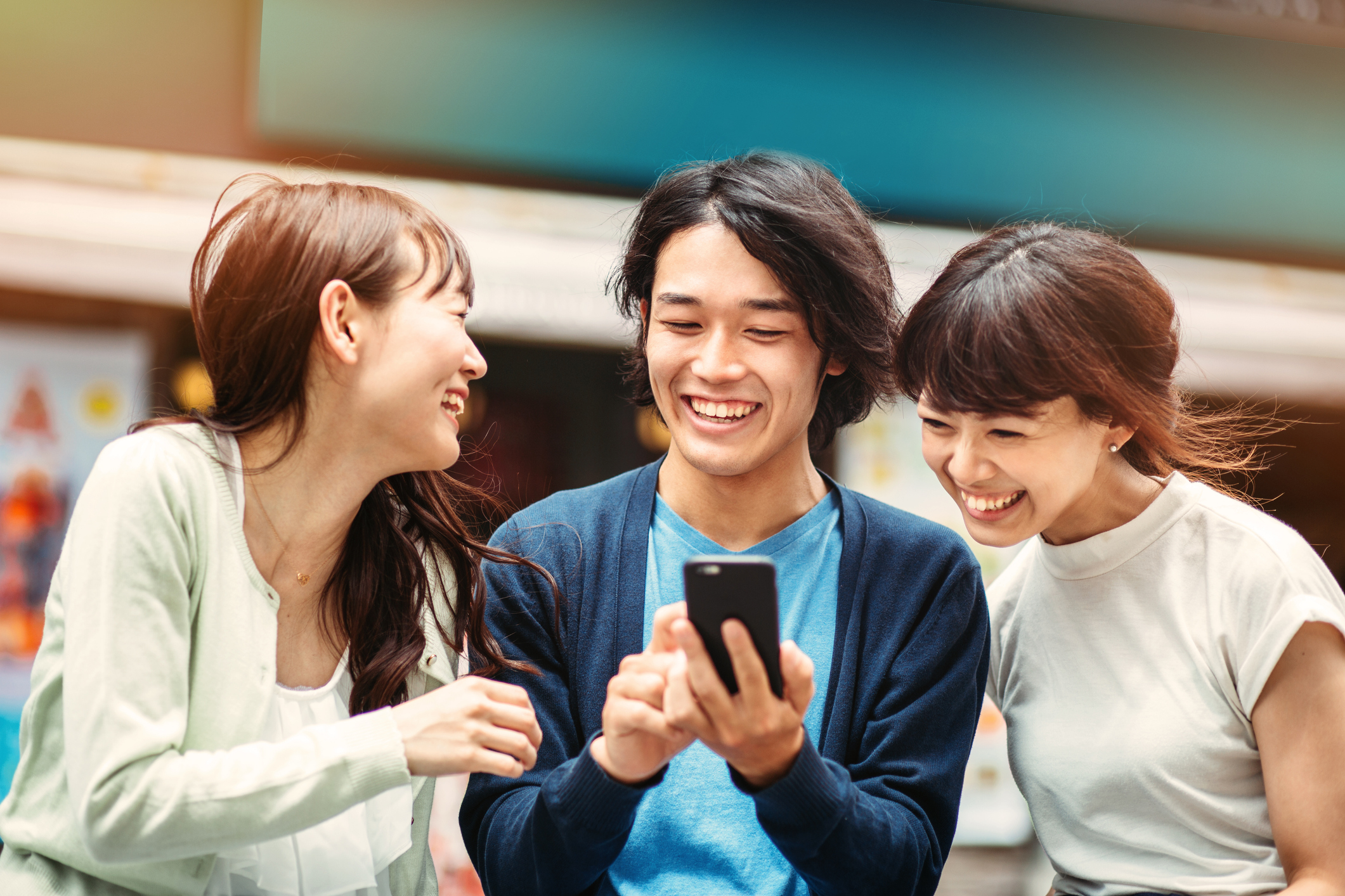 Three teenagers outside looking at a smartphone and smiling.