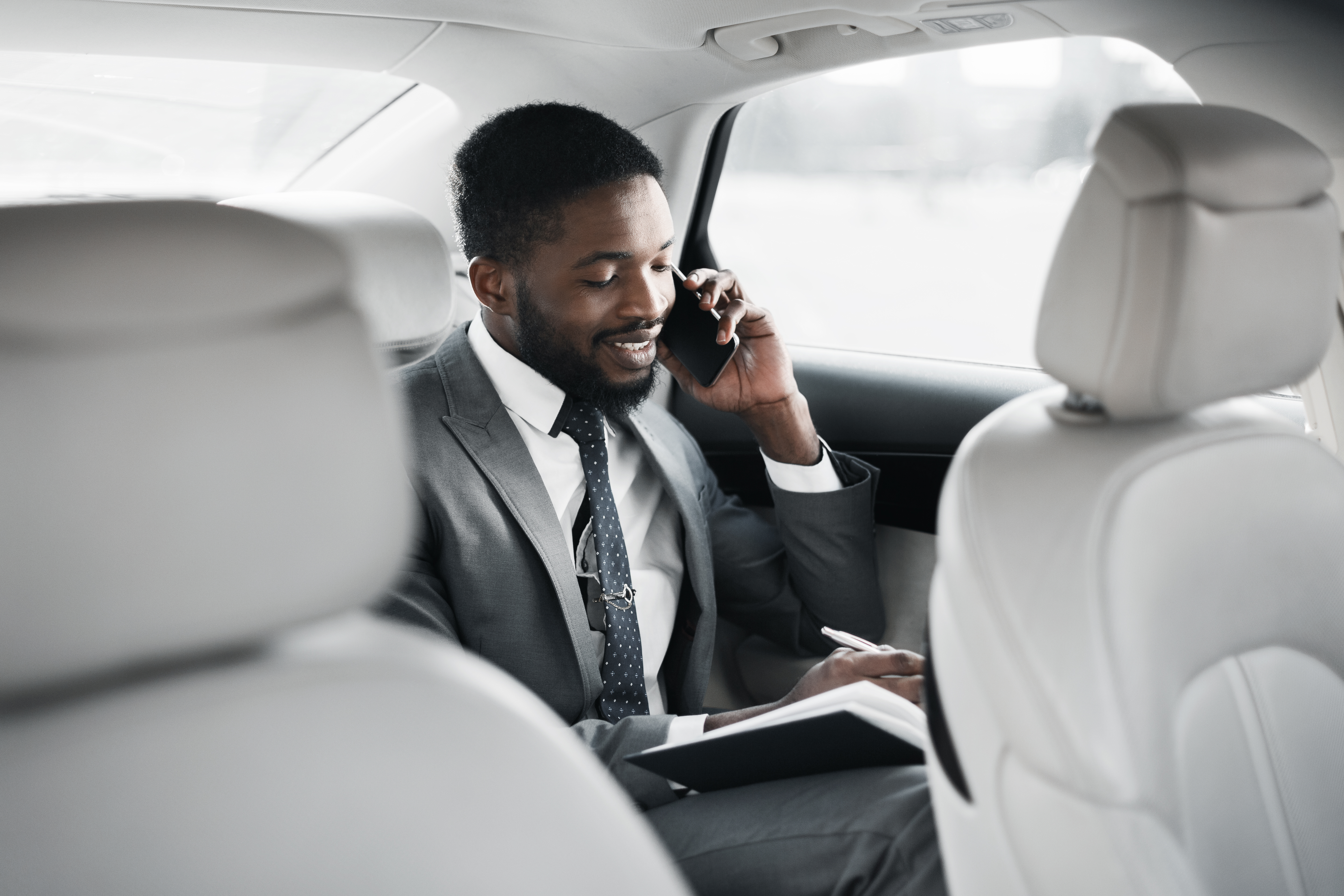 Man in a suit talks on phone while in back of car.