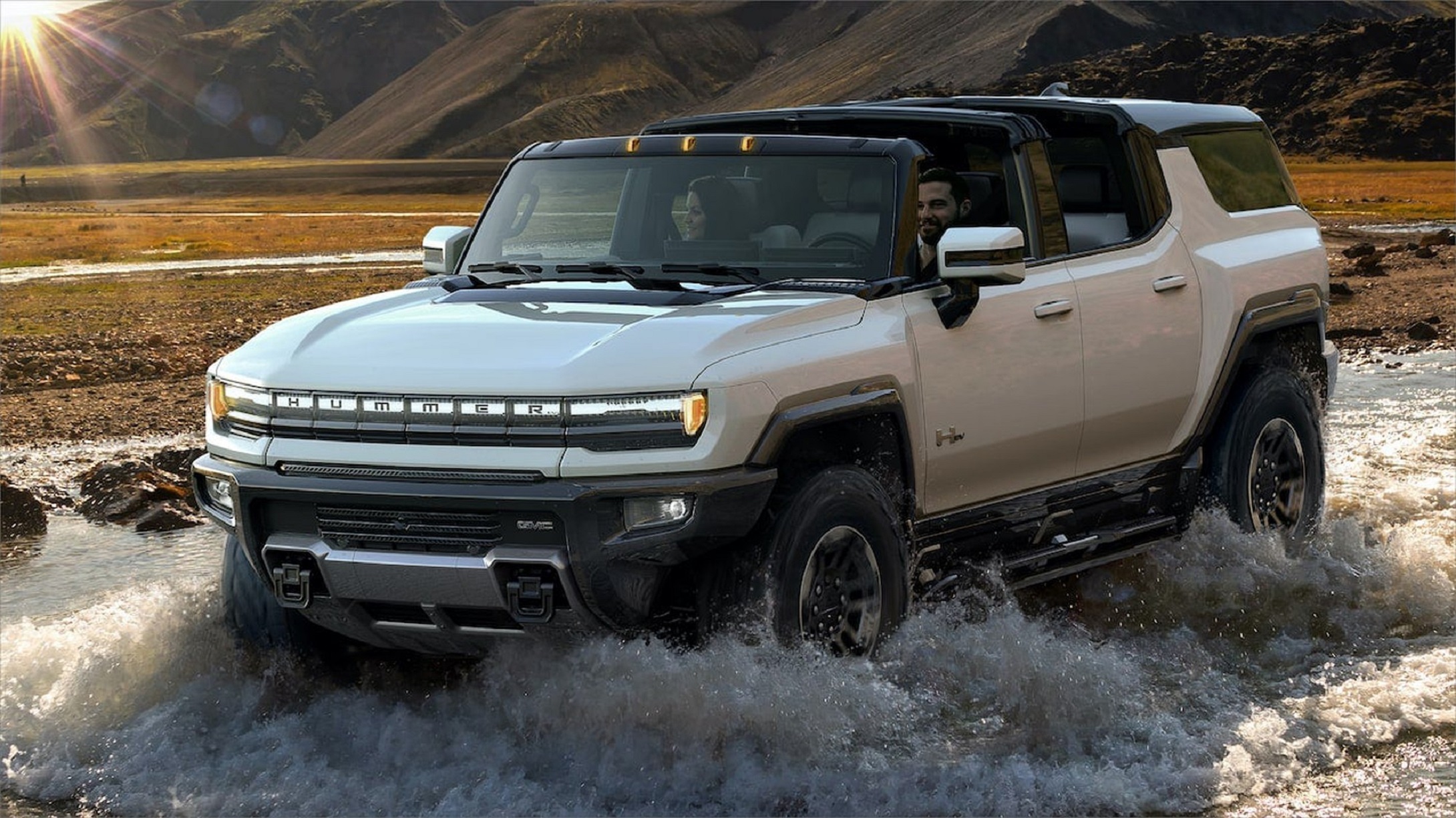 An all-electric GMC Hummer driving through a shallow river.