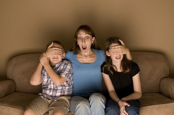 Mother covers the eyes of her two kids while watching TV. 