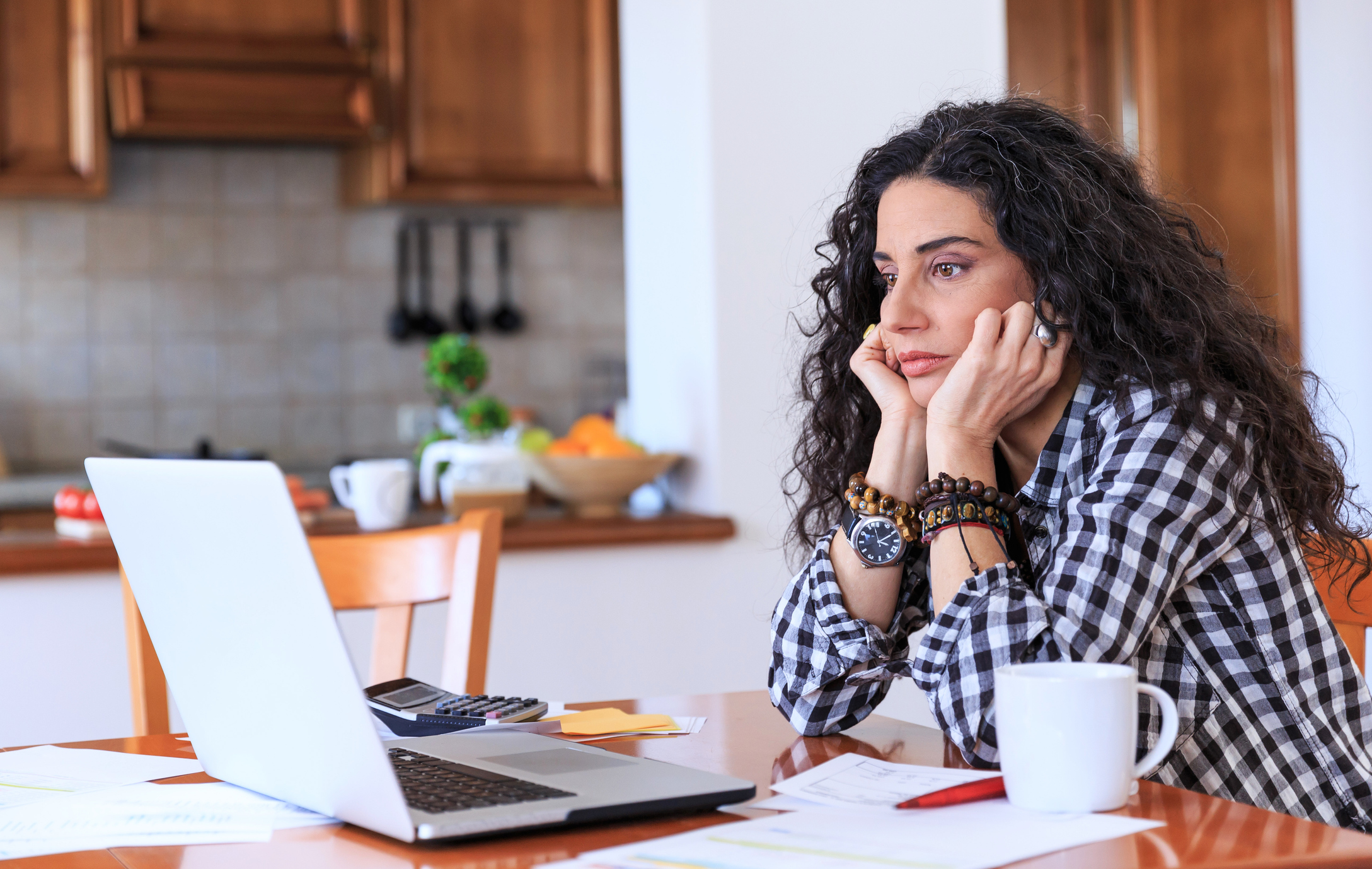 Worried-looking person stares at a laptop in a kitchen setting.