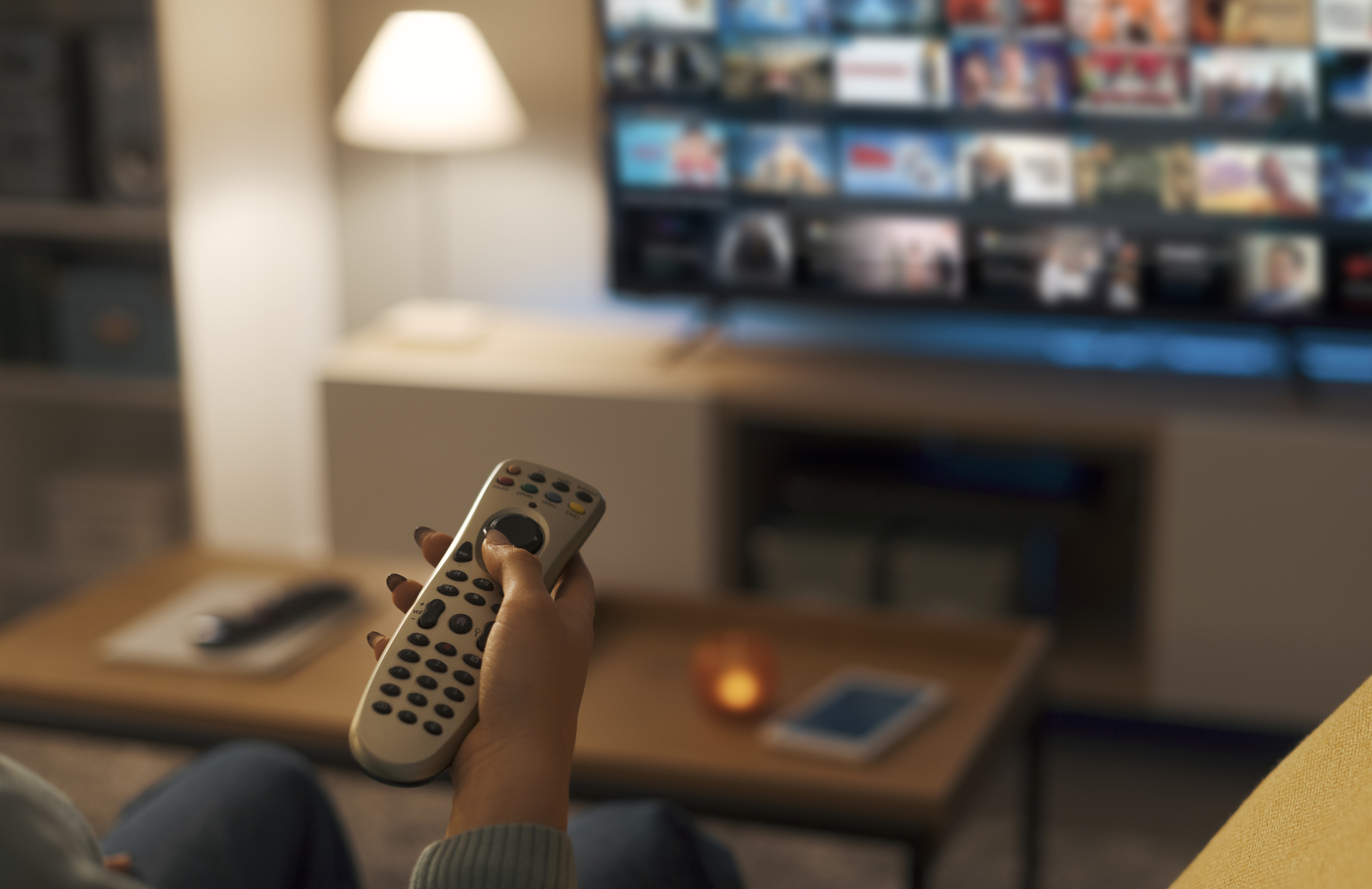 A hand holding a remote pointed at TV.