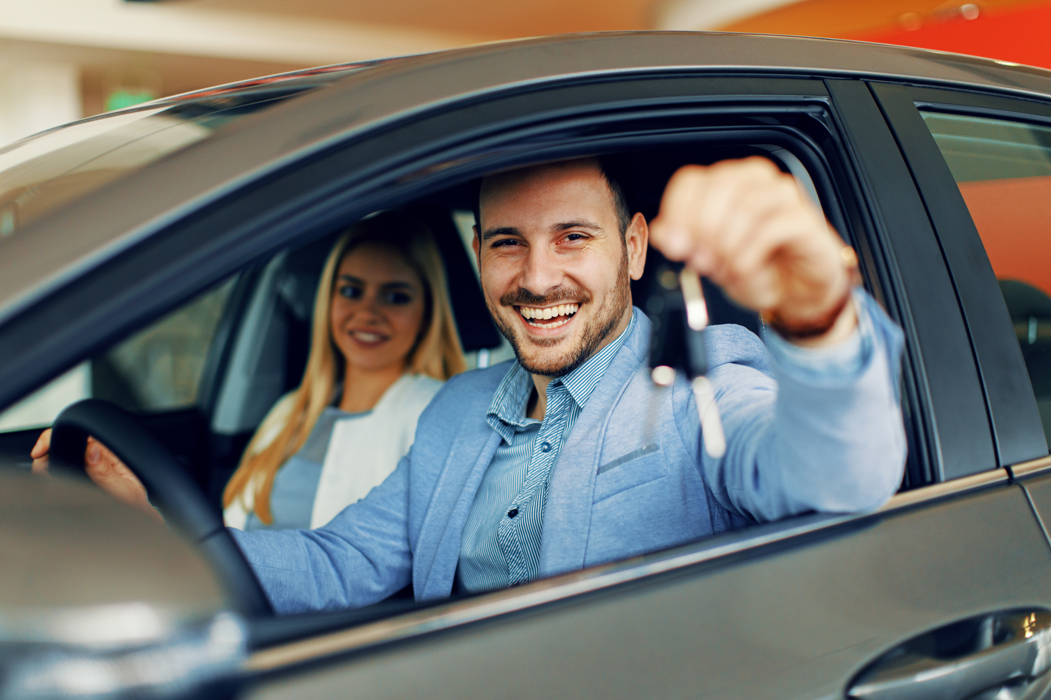 Two people sitting in a car. The driver holds the car keys out the window.