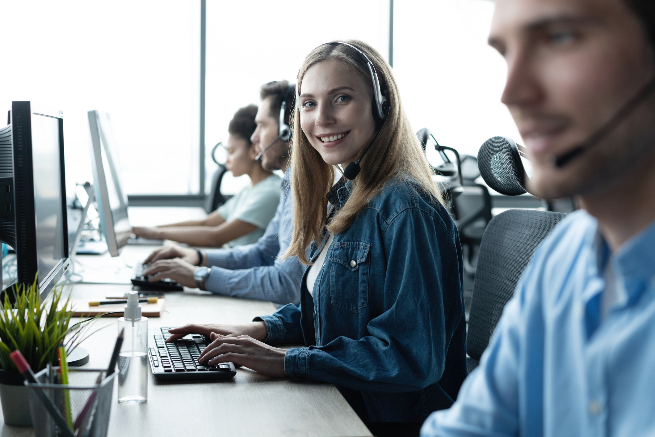 Four people sitting at a counter, in front of computer screens, wearing headsets.