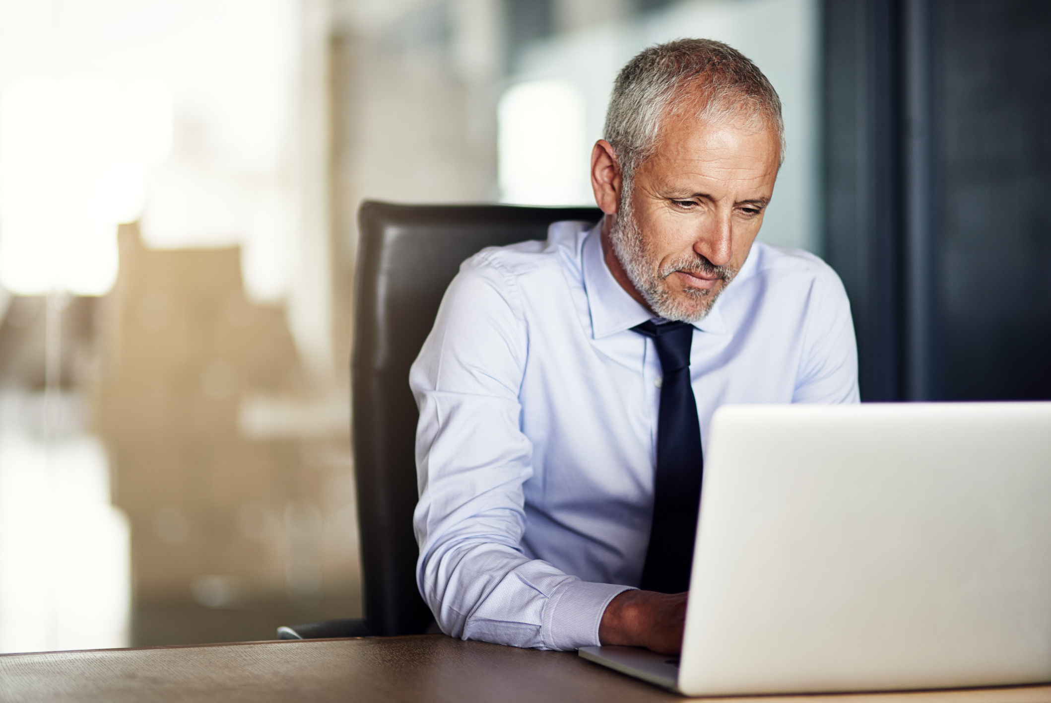 A person in collared shirt and tie working on a laptop.