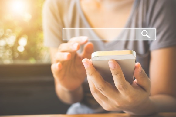 Person looking at a cellphone screen wth a search bar superimposed on the image.
