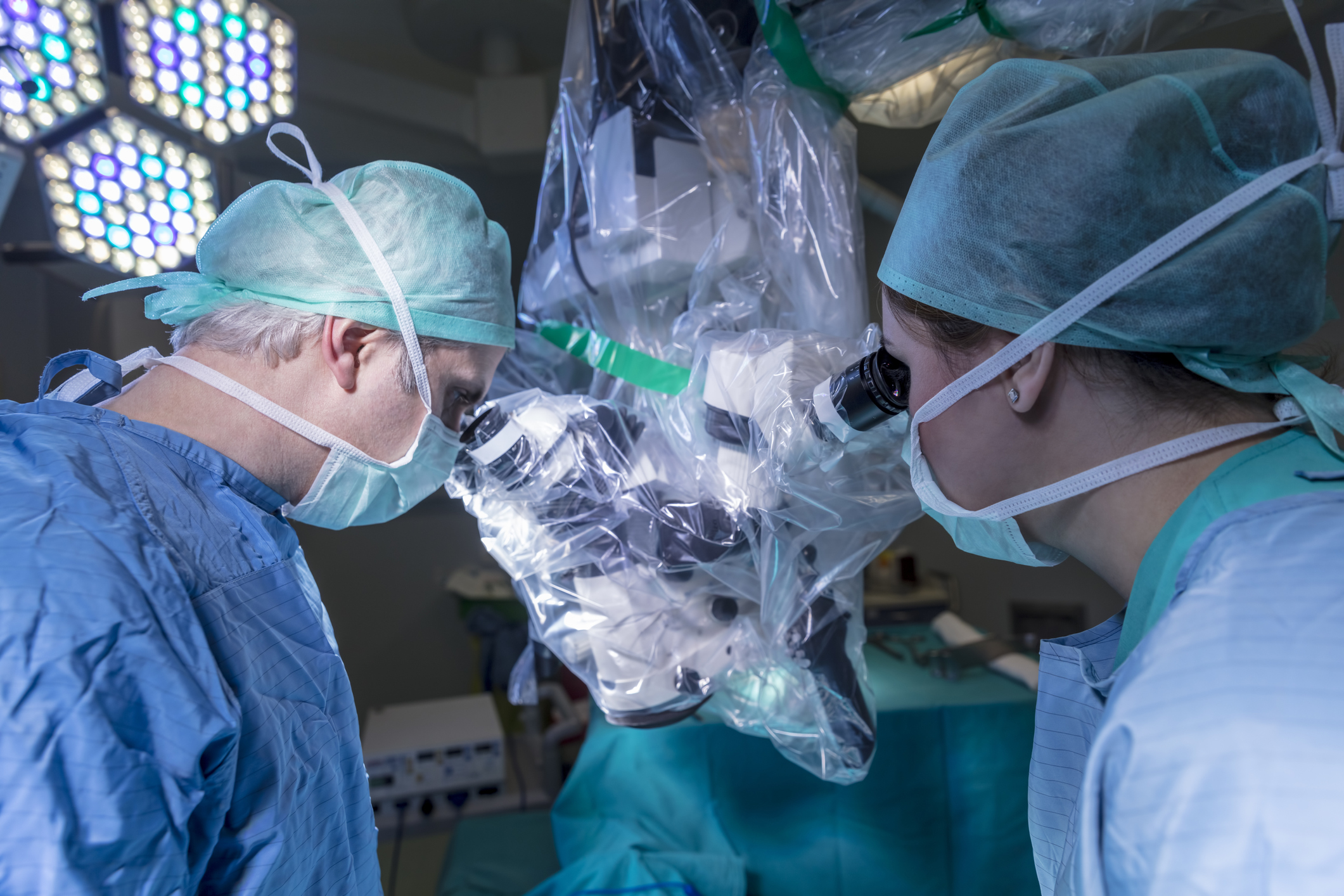 A surgeon peers into a viewfinder while performing surgery with the help of a nurse and a surgical robot.