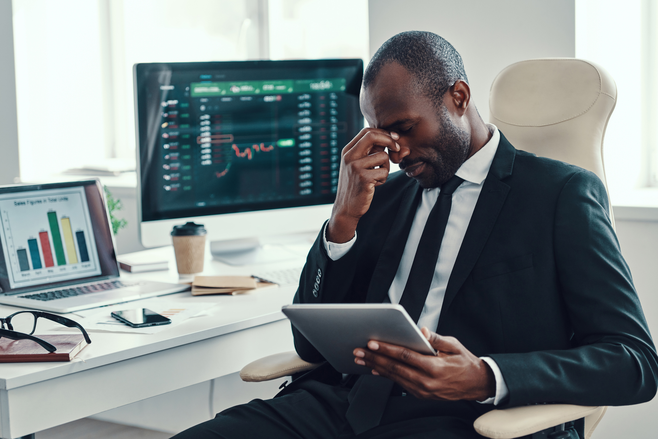 visibly tired and frustrated investor holding tablet in front of stock chart