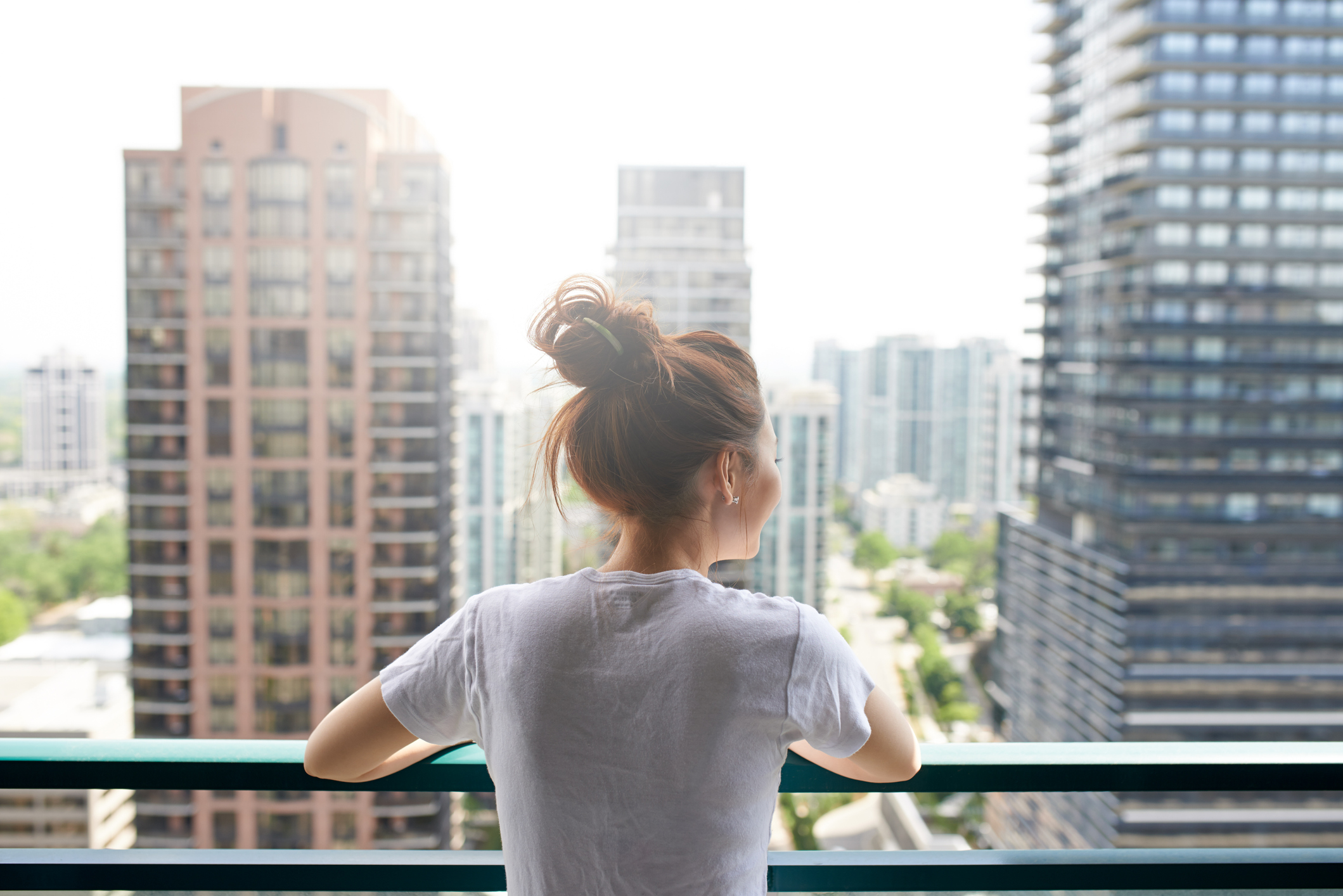 Person on balcony looking at large buildings in a city.