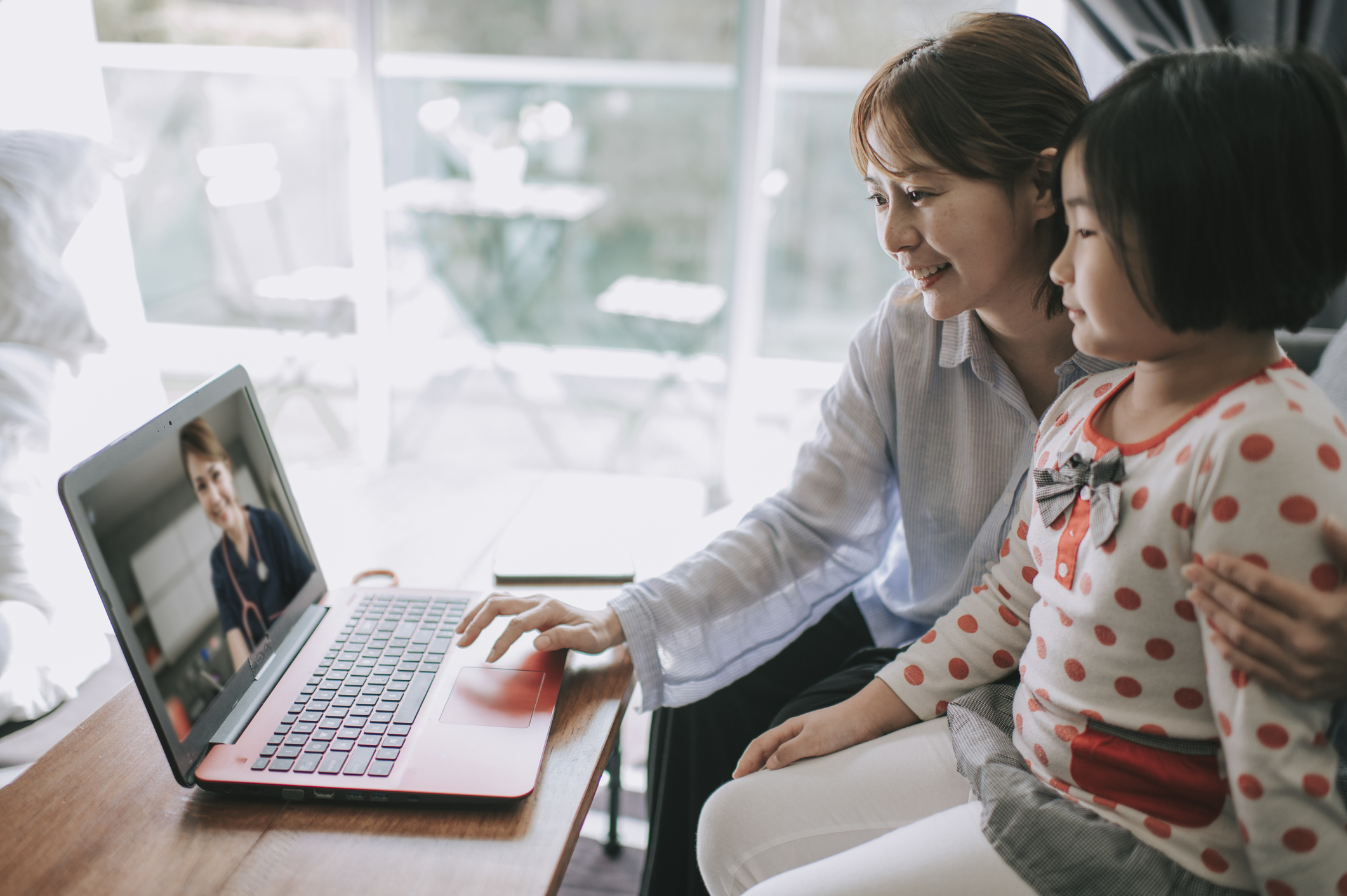 An adult and child visit with a doctor using a telehealth platform on a laptop.
