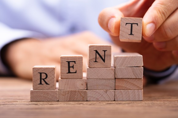 A rising stack of blocks with a person placing letters spelling rent on them.