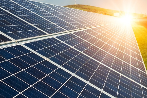 Long line of solar panels laid out against a sunrise.
