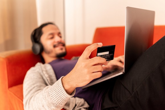 Person reclining on a couch and shopping online with a credit card.