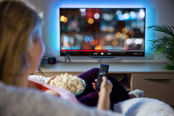A person sitting on a couch watching TV with a remote and popcorn.