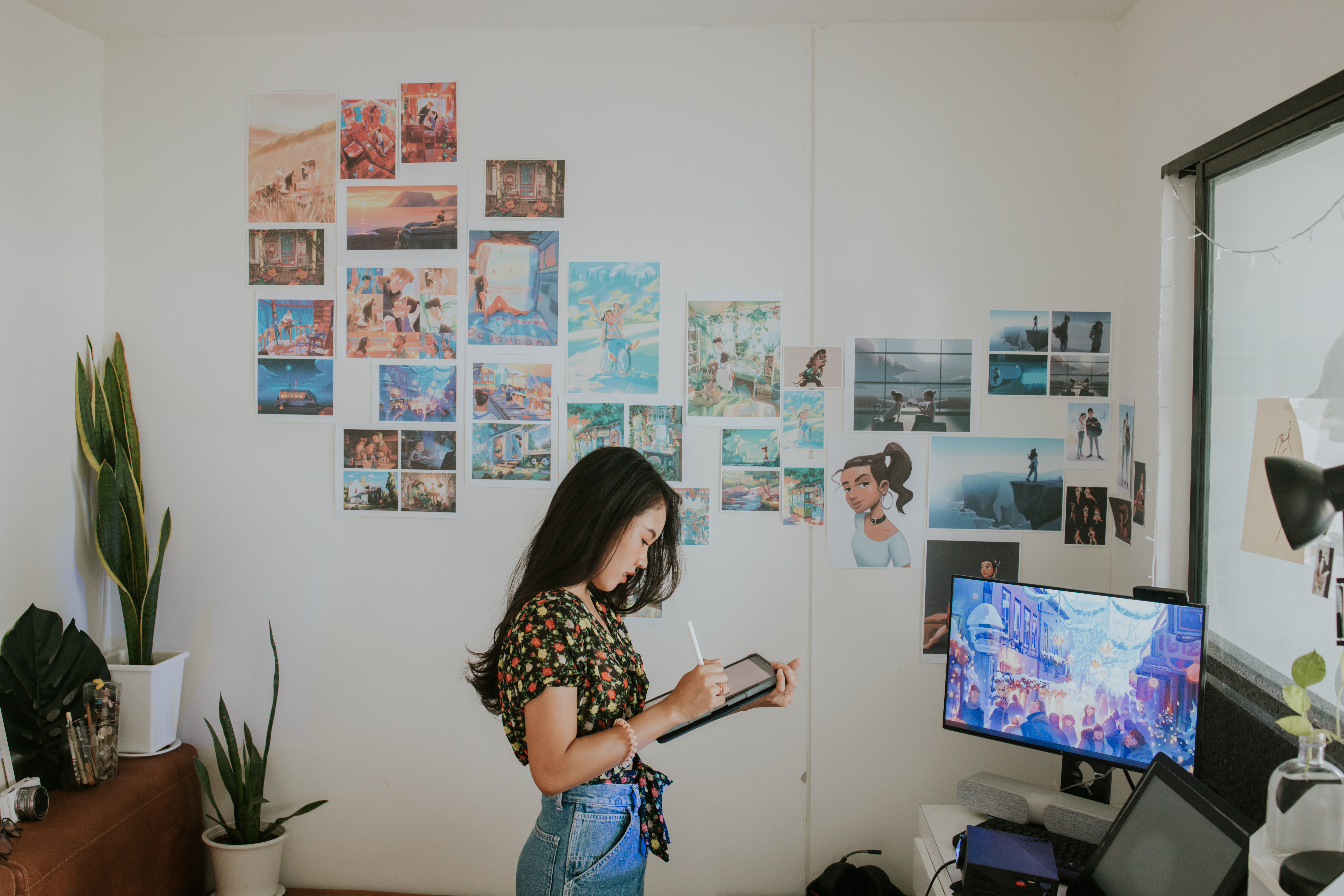 Person in an office with art on the wall, using a tablet and a large computer monitor.
