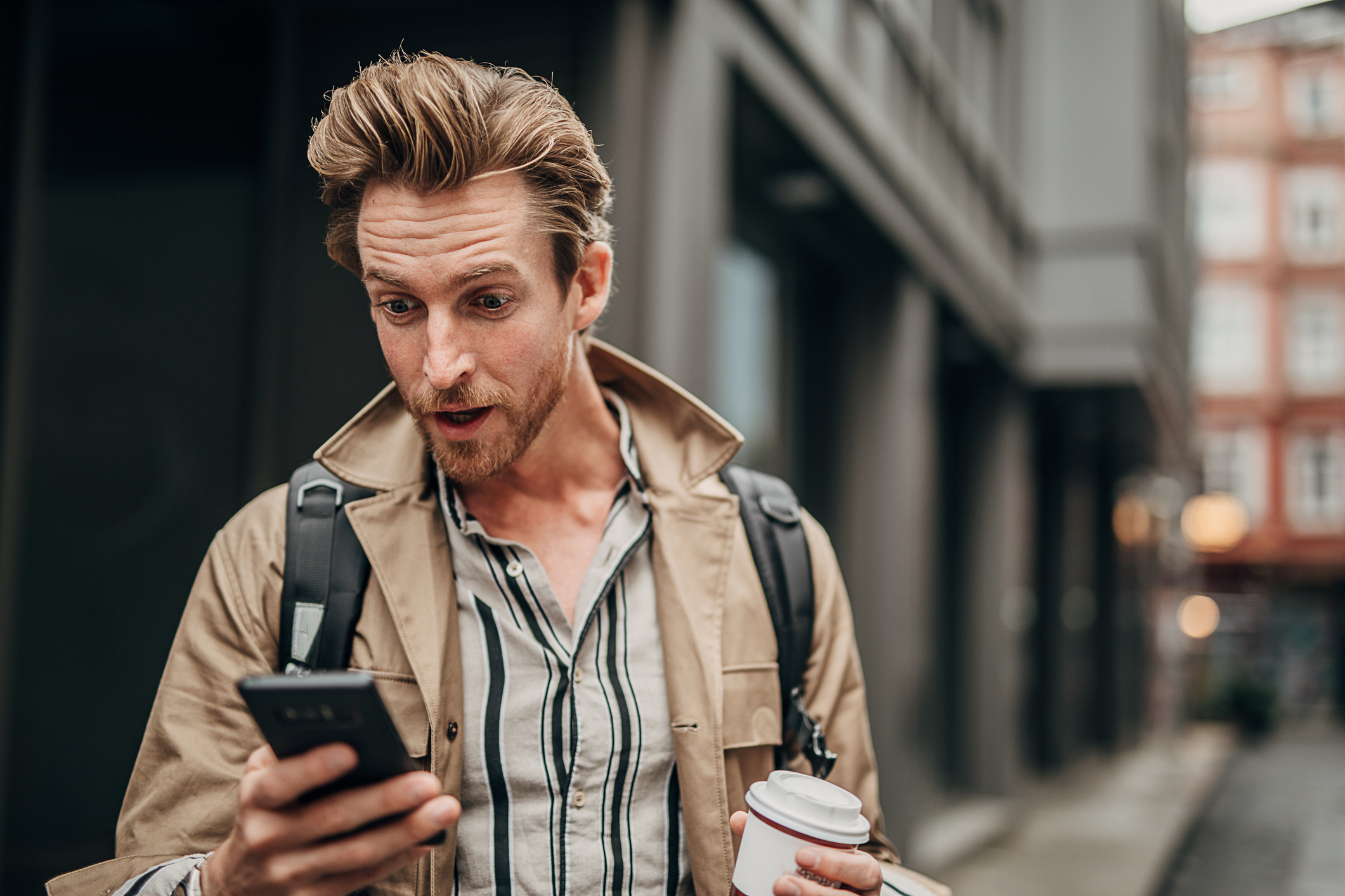 A person looking at their phone on the street with a surprised look on their face.