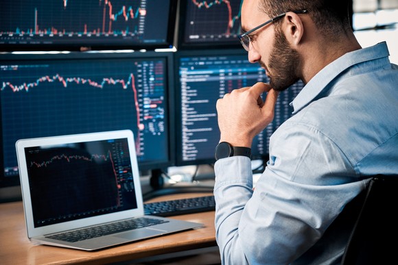Concerned person looking at a laptop, which is backed by a bank of PC monitors.