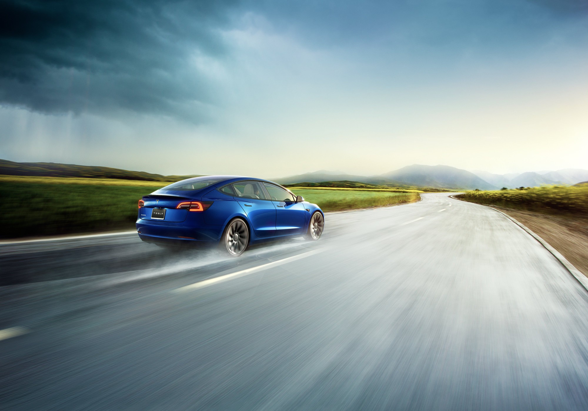 A tesla car driving fast through the rain on an open road
