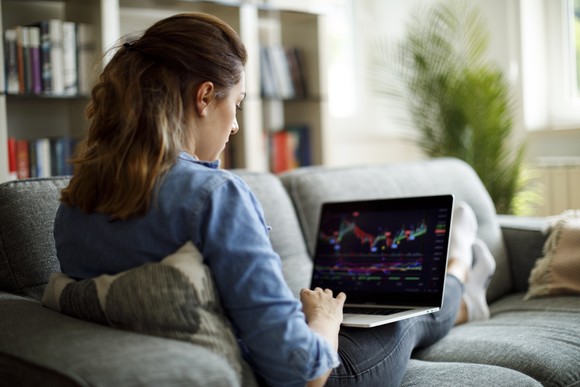 A person on a couch looking at stock charts on a computer.