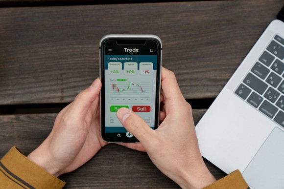 Person holding a smartphone with a stock chart on the screen.