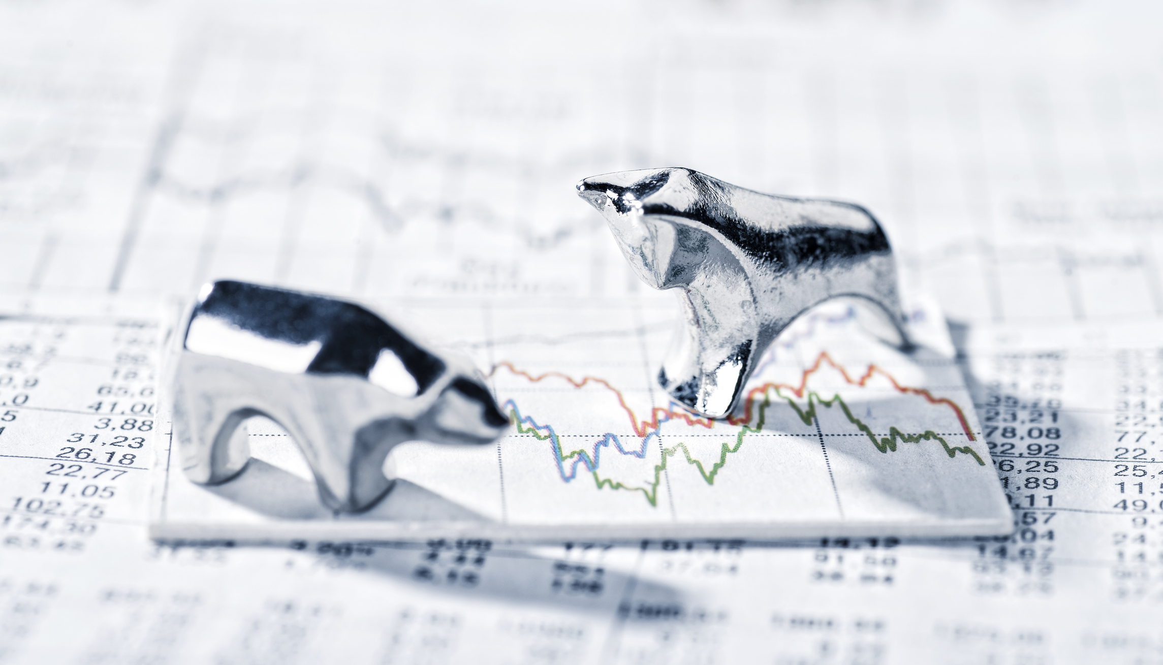 Metallic bull and bear placed on a chart on top of stock tables in newspaper.