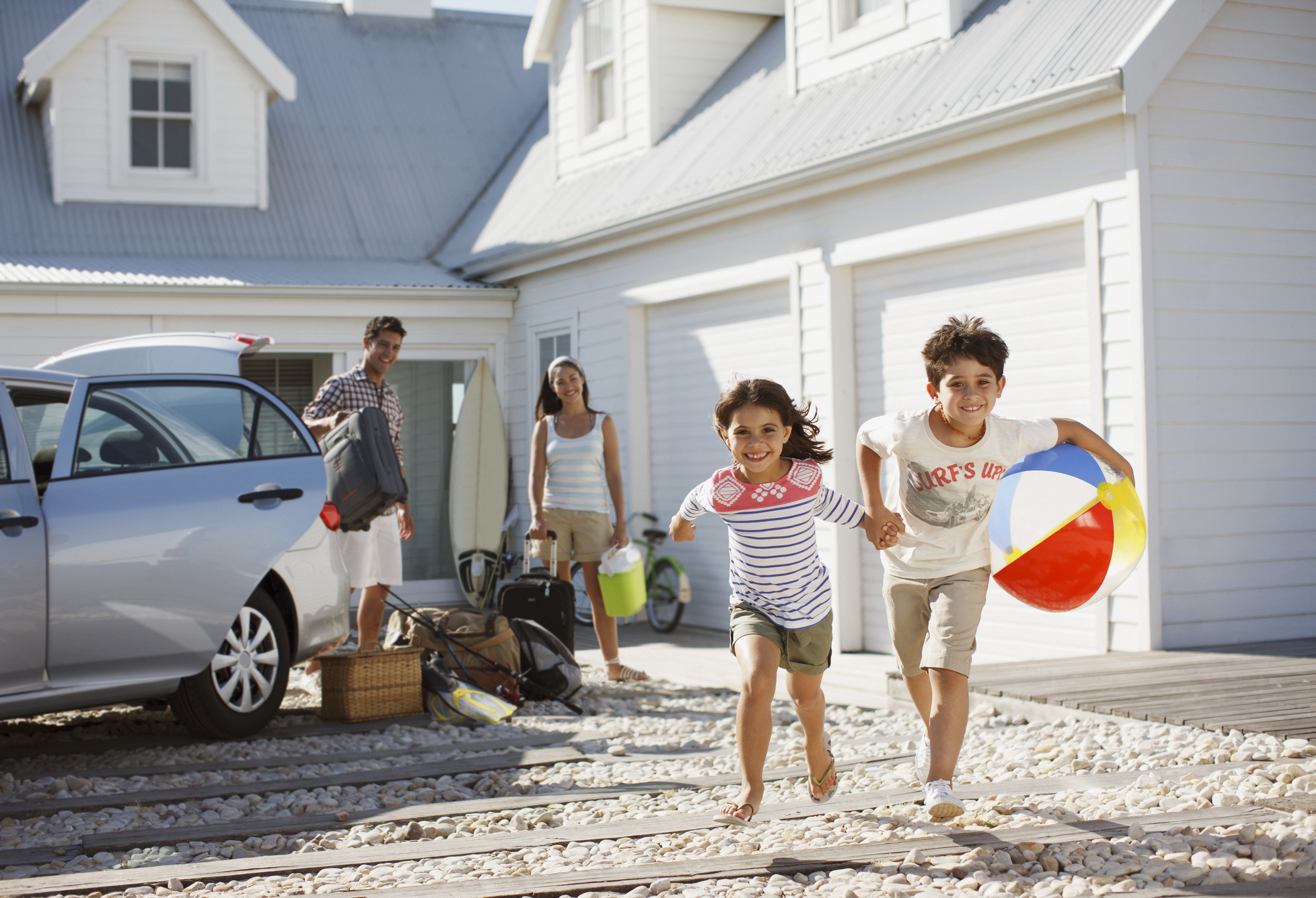 Kids running outside a beach house as parents observe.
