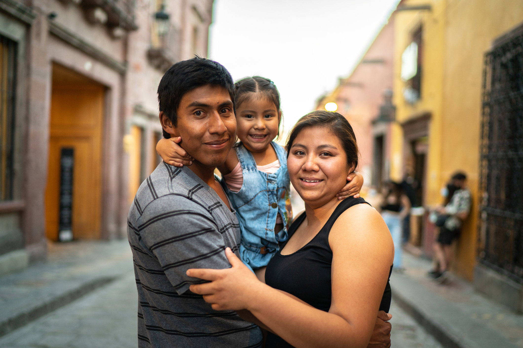 Two parents holding their small child outside in a city.