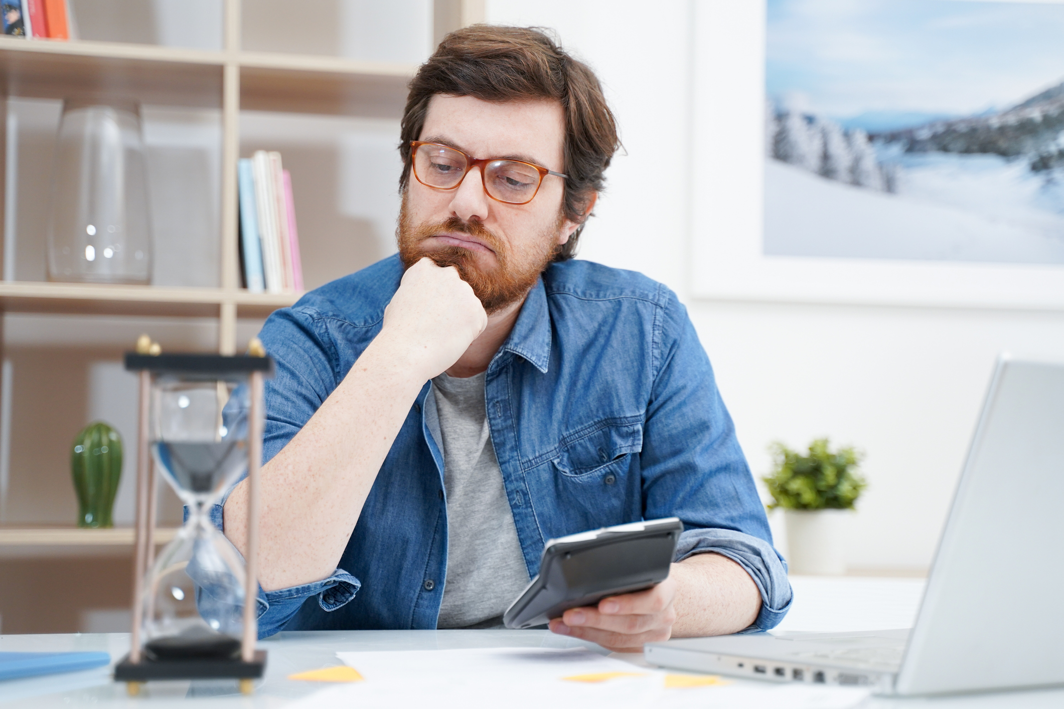 Person looking at hourglass while holding calculator.