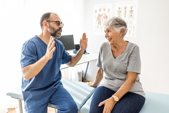 A person in scrubs gestures at a seated person.