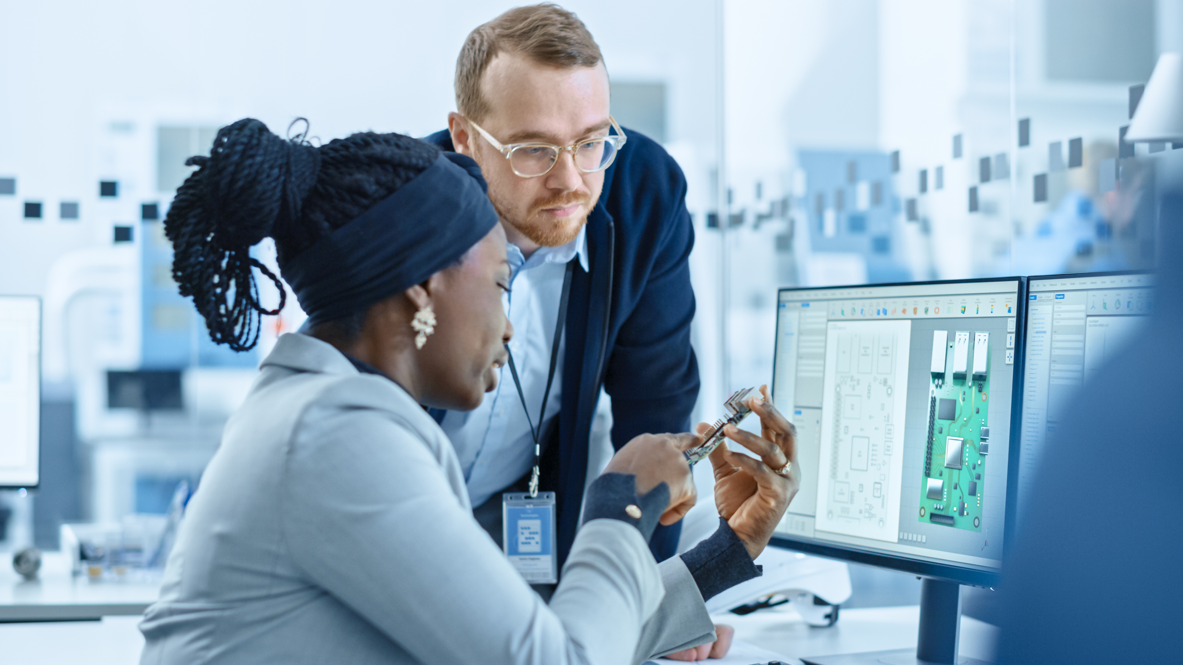 Two people looking at semiconductor design on computer and in hand.