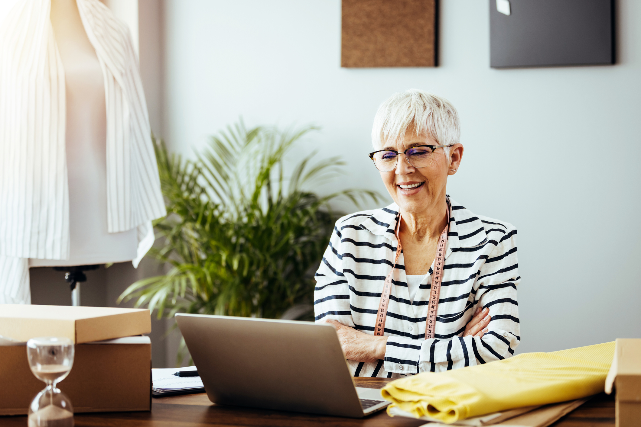 A smiling person with arms folded looking at a laptop.