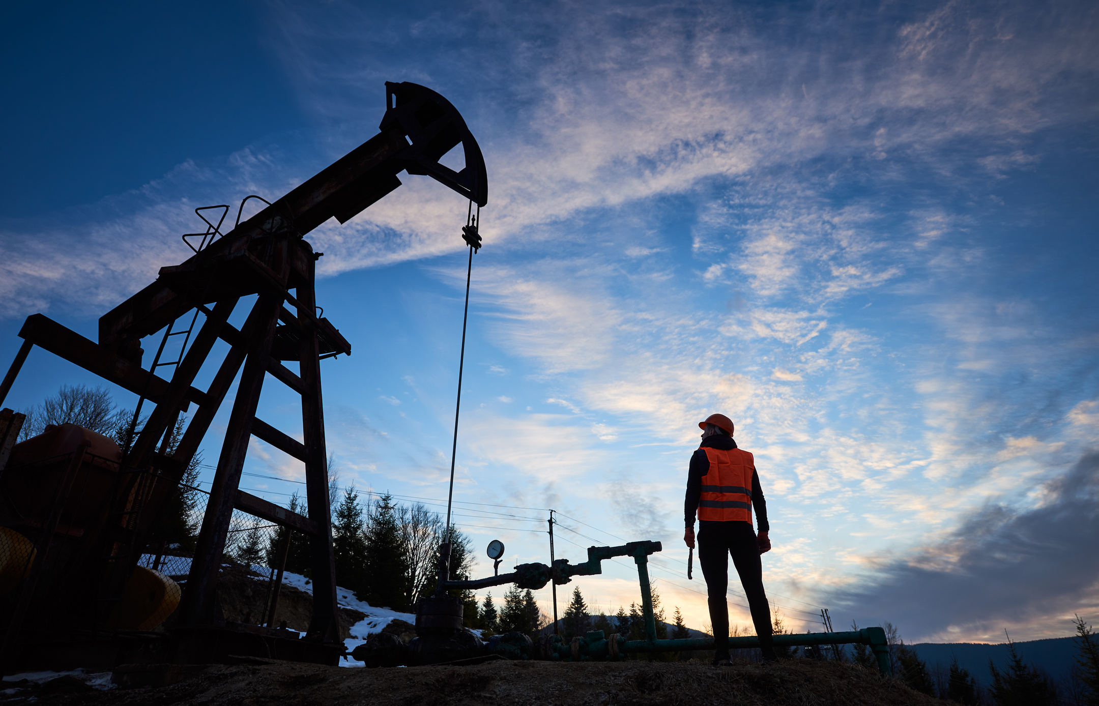 The silhouette of a person next to an oil well.
