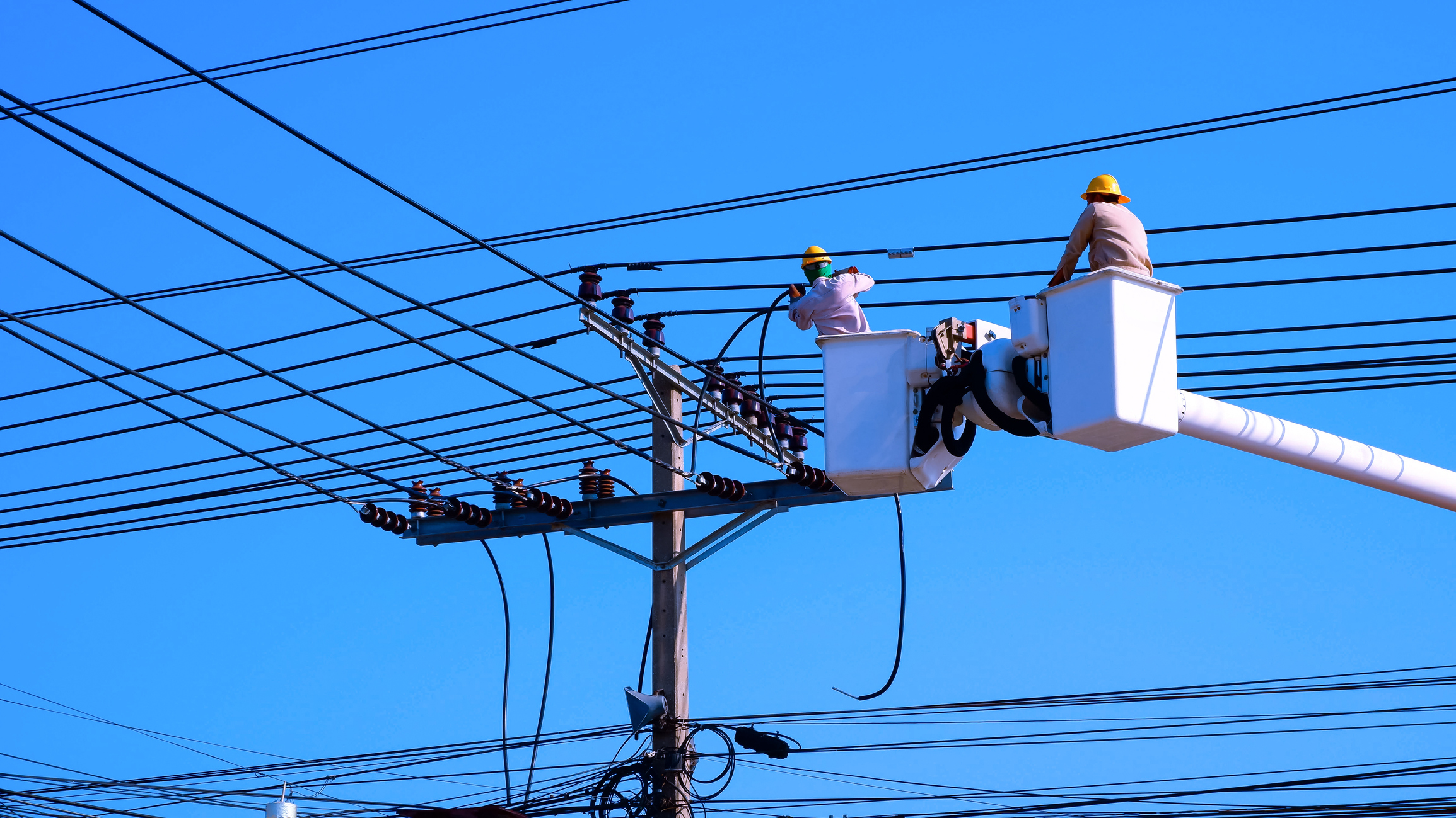 Two technicians service electric power lines with a deep blue sky in the background.