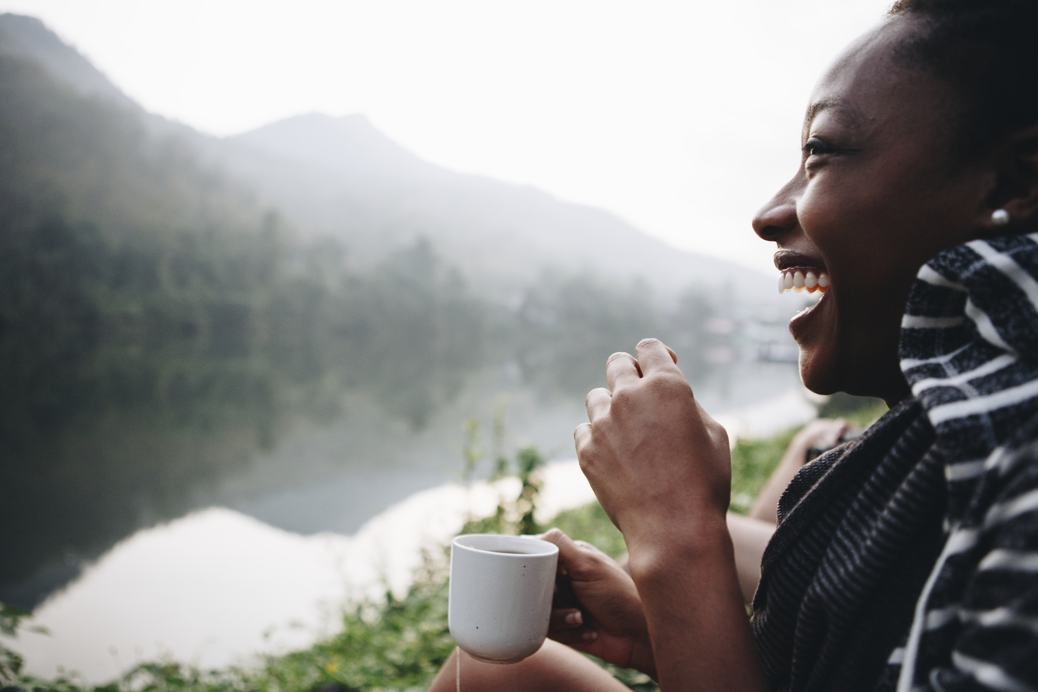 A person smiles while enjoying a cup of coffee in the morning, overlooking a forest.