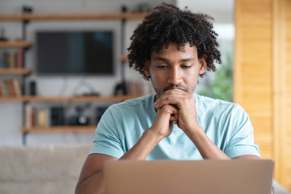 An investor looks thoughtfully at a laptop in a living room setting.