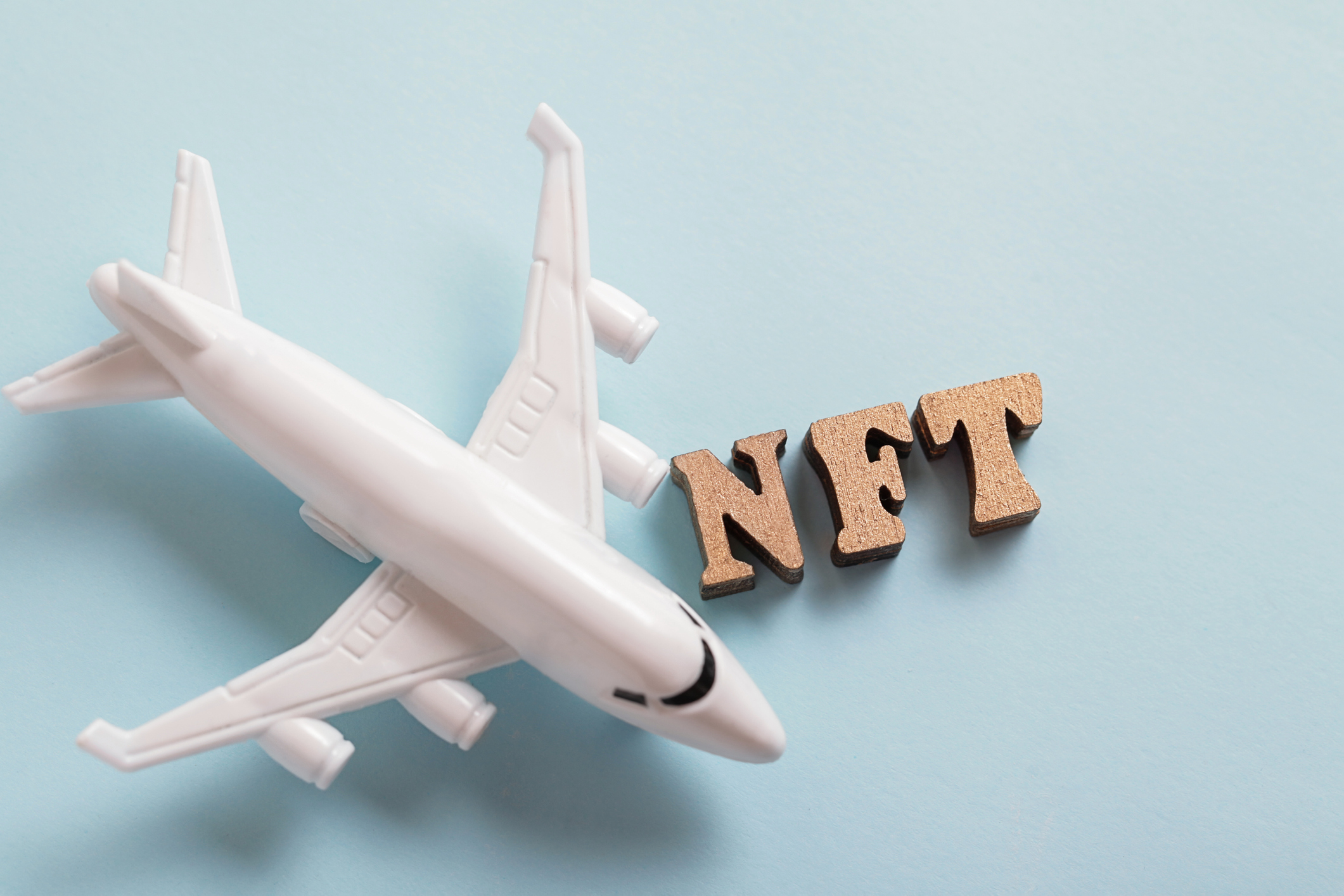 Model white airplane beside the letters NFT on a pale blue background.