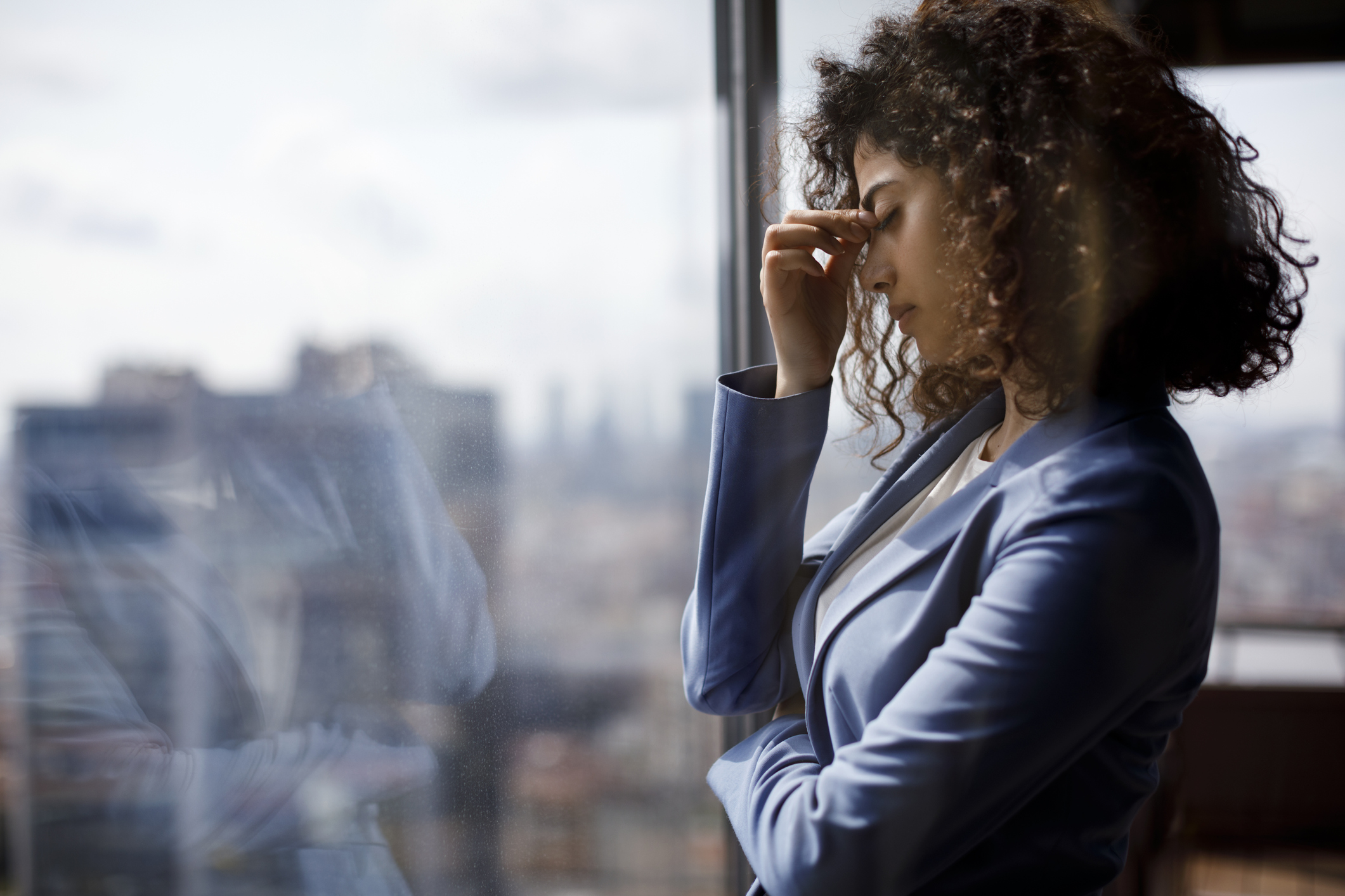 A stressed-looking investor stands by a large window and pinches their brow.