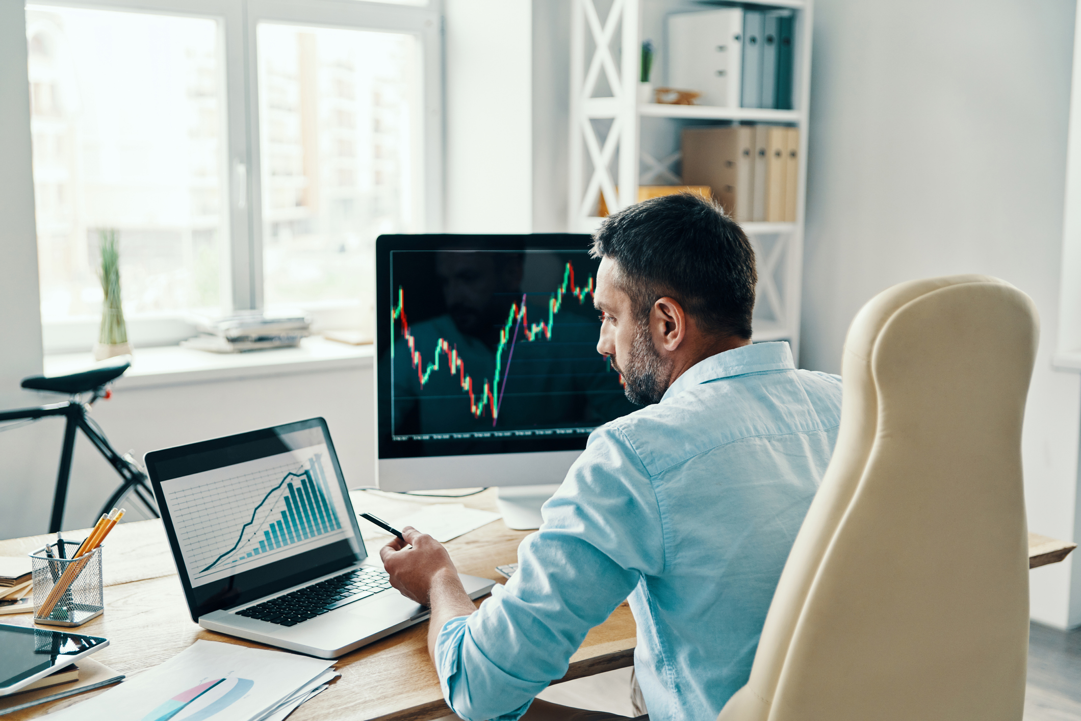 A person is looking at stock charts and other financial information on computers while sitting at a desk.