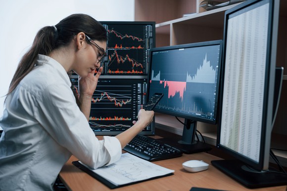 A person is looking at business metrics and stock charts on computers. 