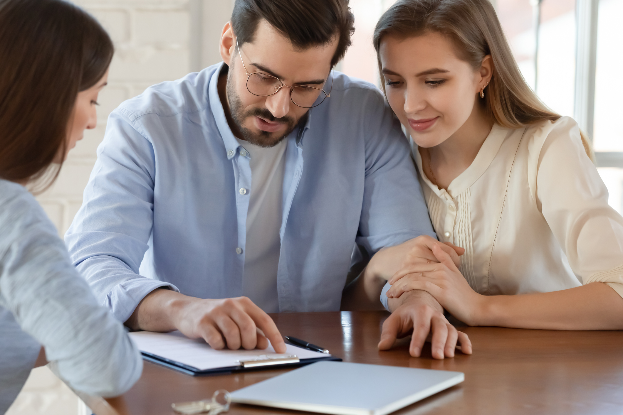 A trio of investors sit around a table while one points to data on a clipboard.