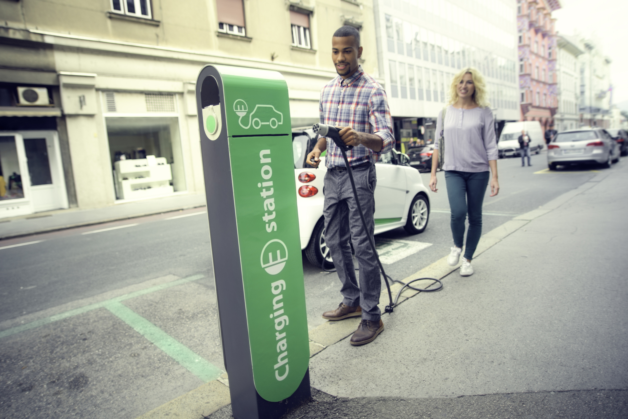 A person holding an electric car charging nozzle at a charging station to charge a car.