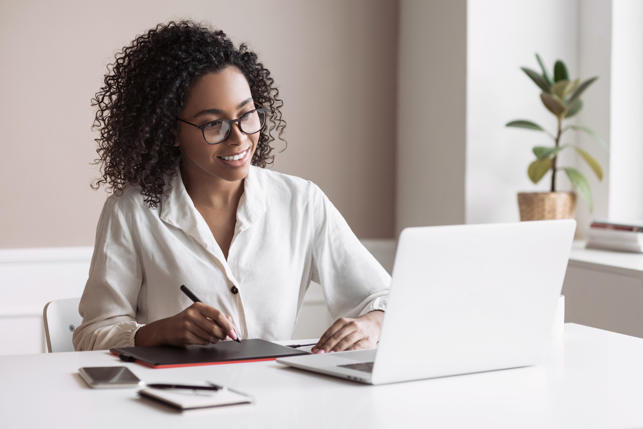 Person smiling at laptop while writing on notepad.