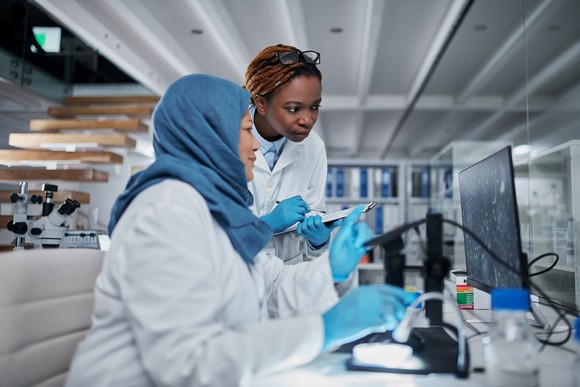Two lab researchers collaborating while using a digital microscope. 