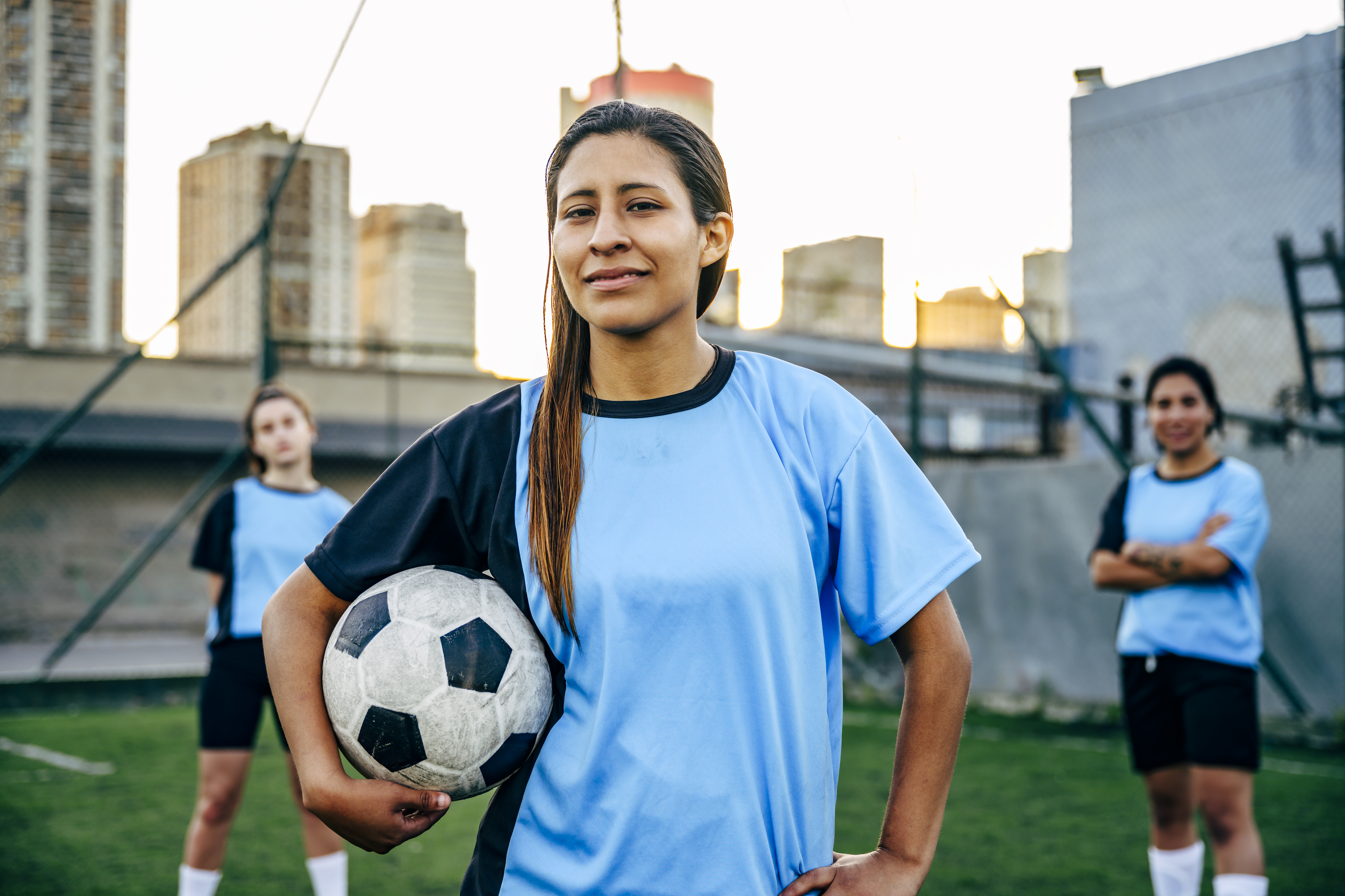 Young soccer player with ball standing with teammates on an urban soccer pitch.