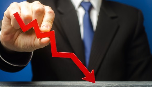A person in a suit and tie  holding a downward pointing red arrow. 