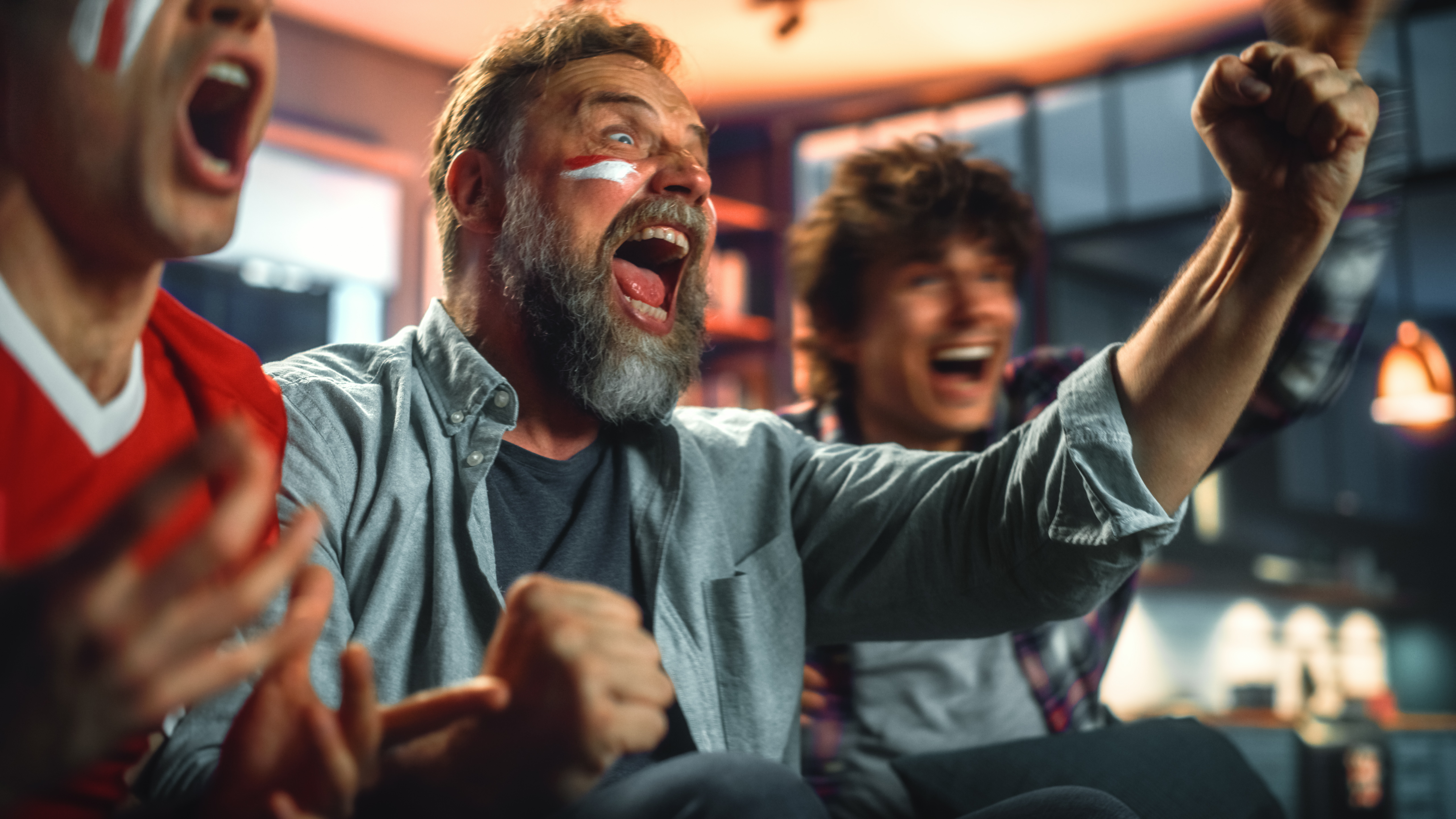 Three people at home, cheering on a sports game.