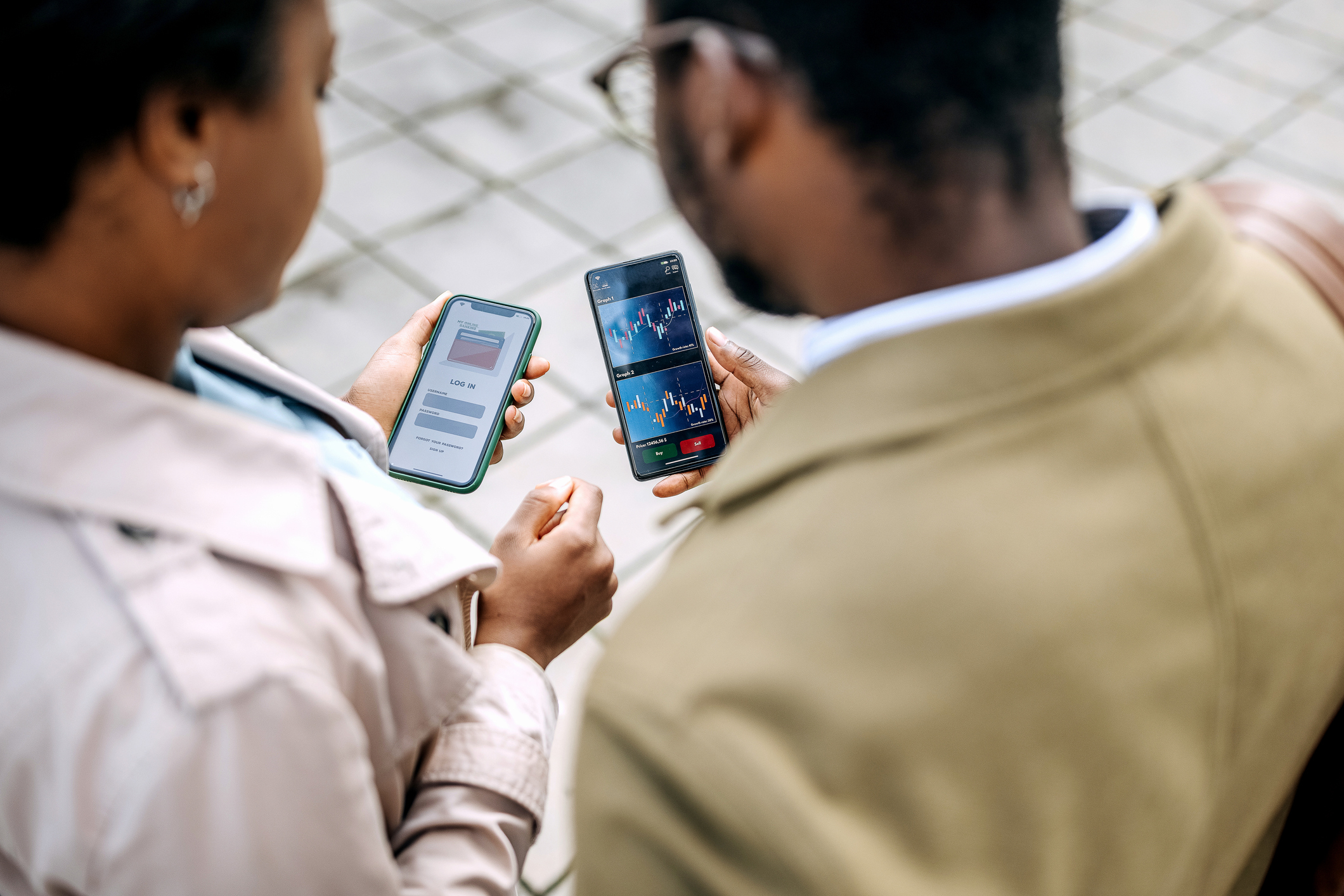Two people standing next to each other looking at their smartphones.