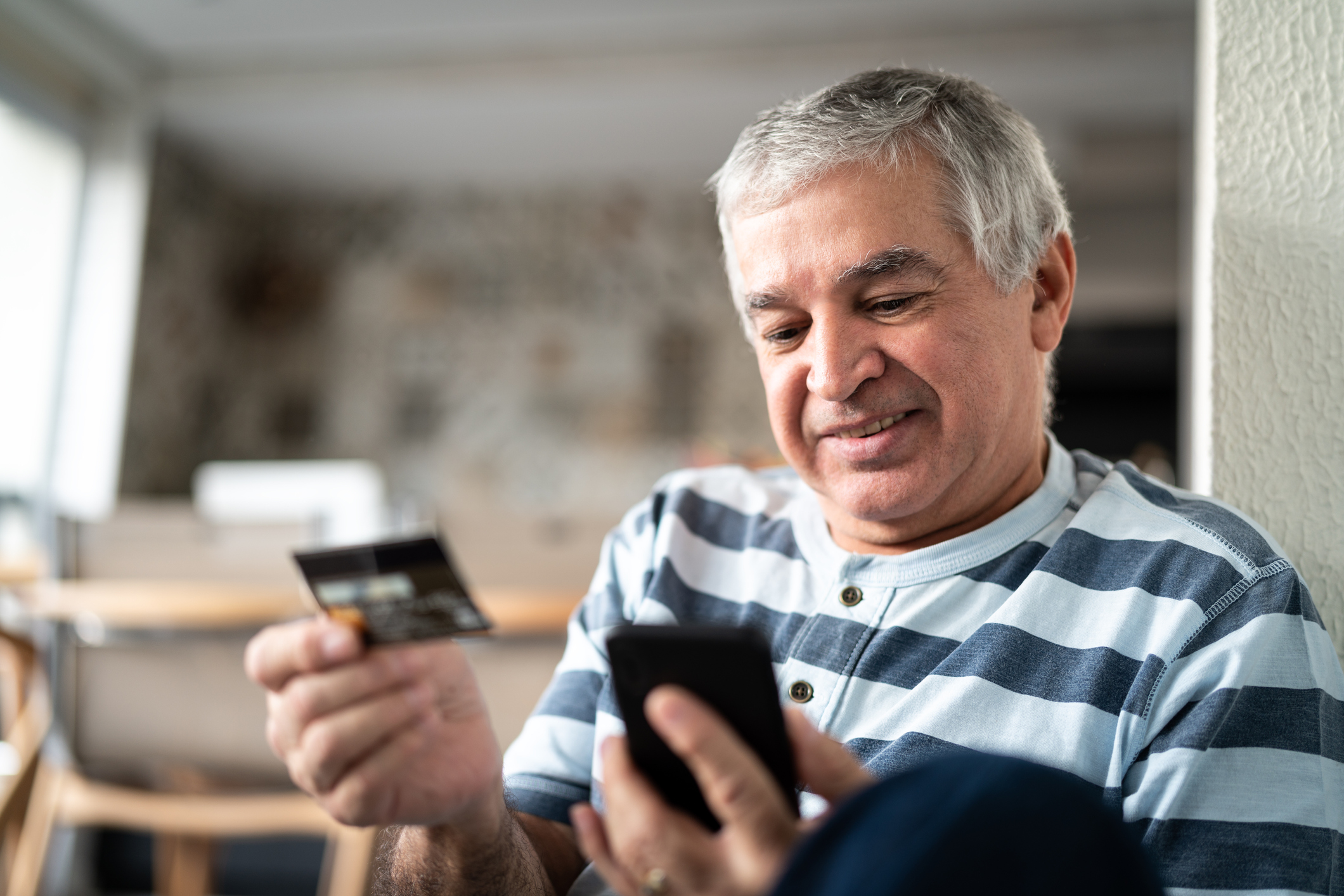 A person holds a credit card while looking at a smartphone.